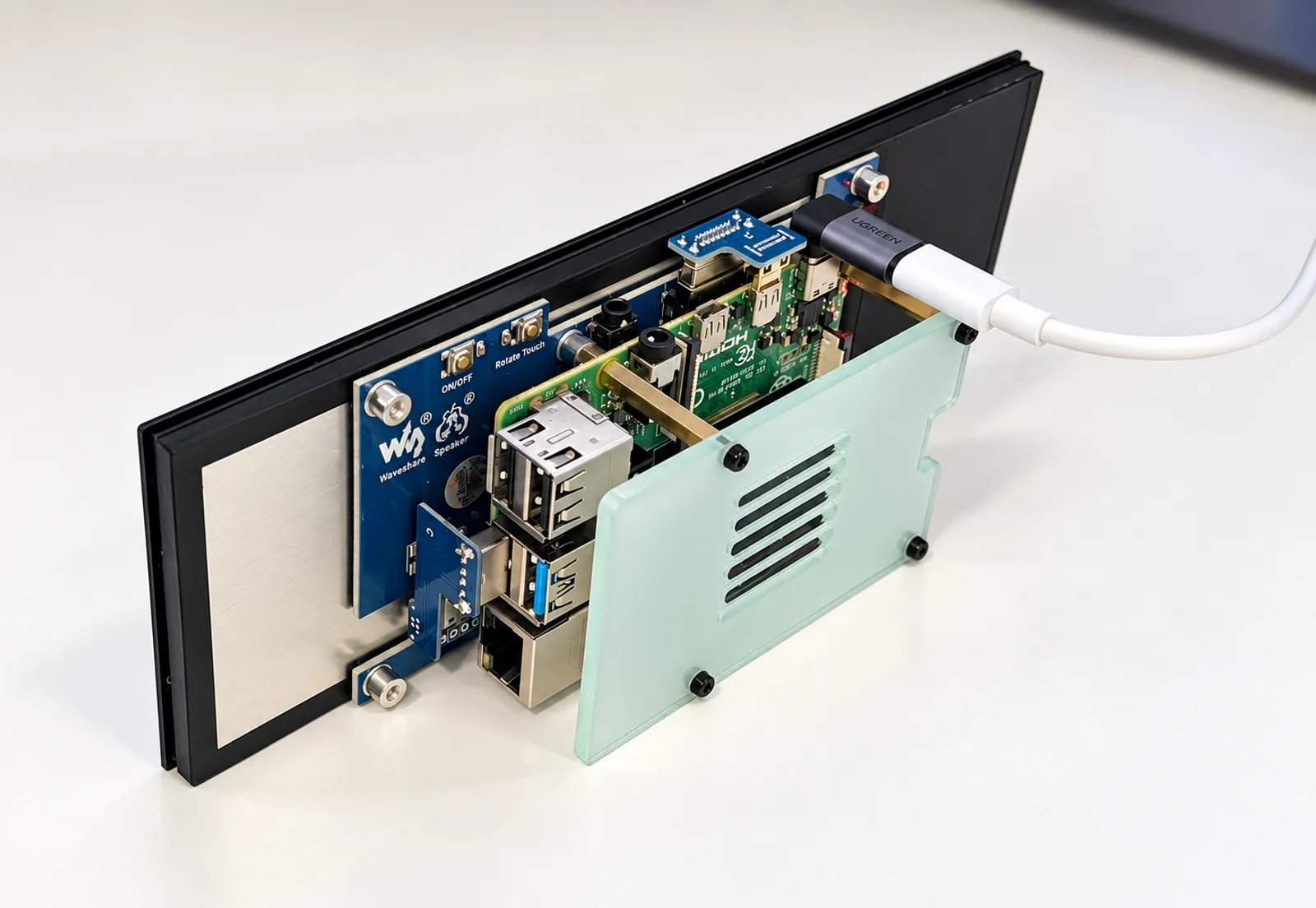 A render of the back of the unit, screen face down on a desk — the panel's blue Waveshare driver board with its ON/OFF and Rotate Touch buttons, and a Raspberry Pi behind a tinted backplate, its USB, Ethernet and HDMI ports exposed and a right-angled USB-C cable going off to the side